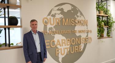 Michael Rea, the Carbon Trust's CEO, in the Carbon Trust office at Arbor in London, next to a mission statement that says "Our mission is to accelerate the move to a decarbonised future"