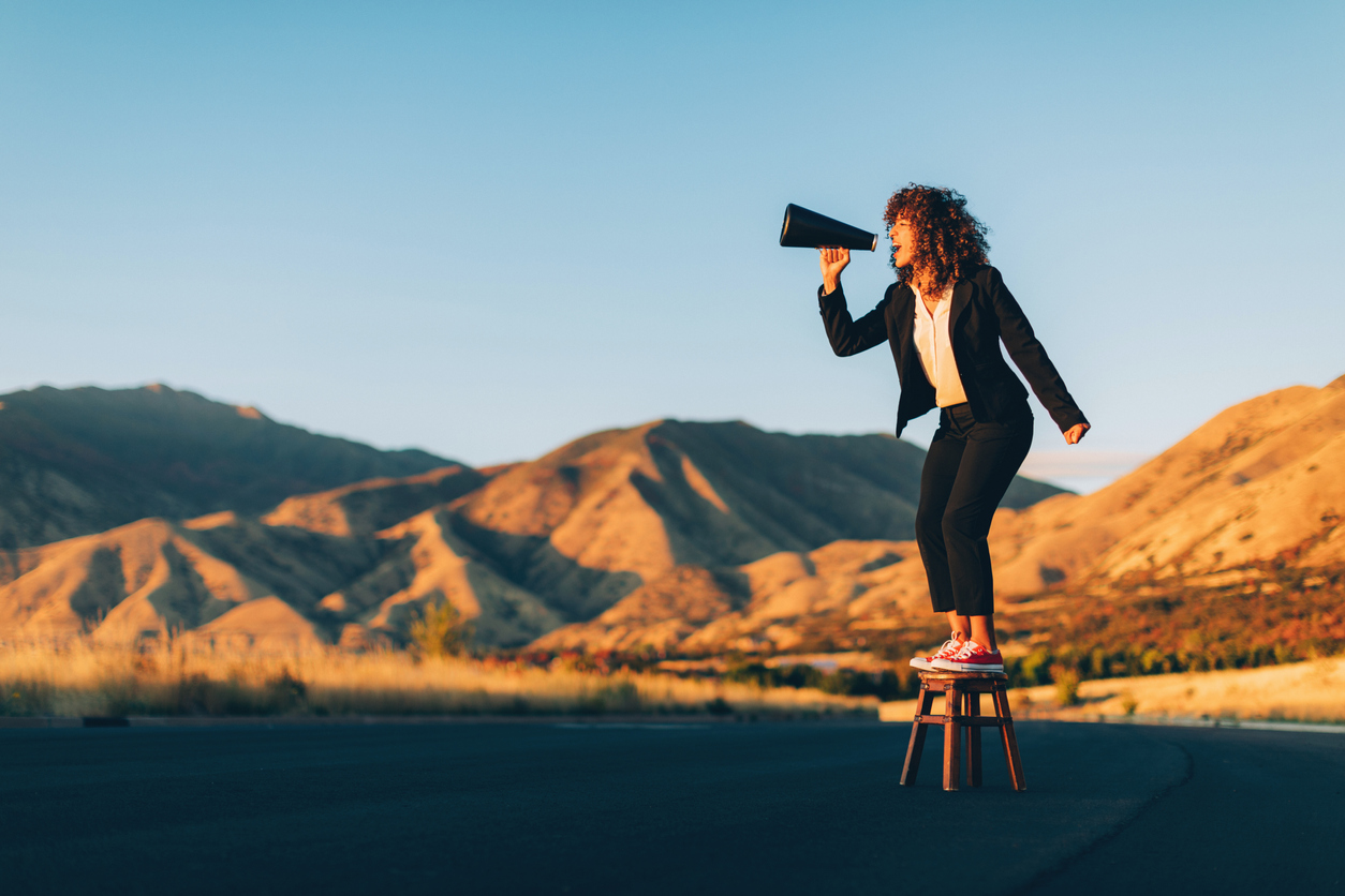 A person standing on a stool, shouting through a loud-speaker