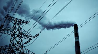 overhead electricity pylon and power lines with a smoking chimney